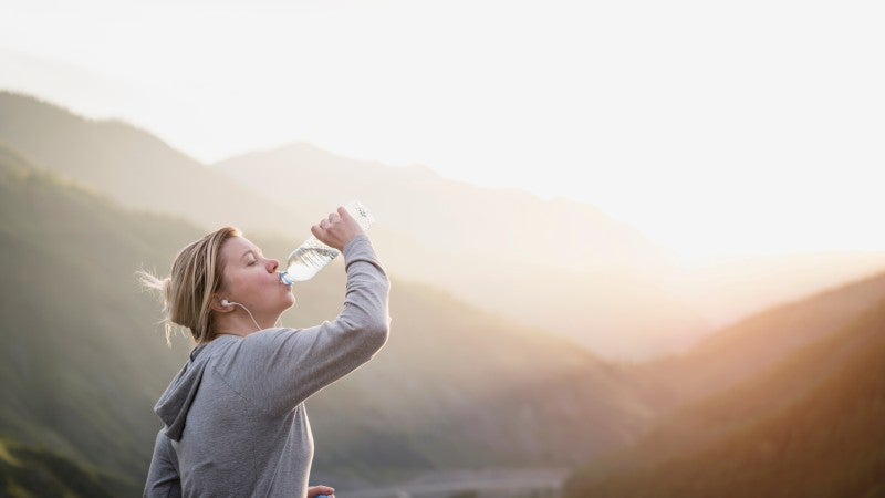 Kvinna dricker vatten vid berg