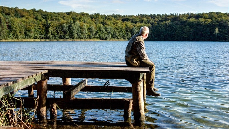 Äldre man sitter på brygga vid en sjö