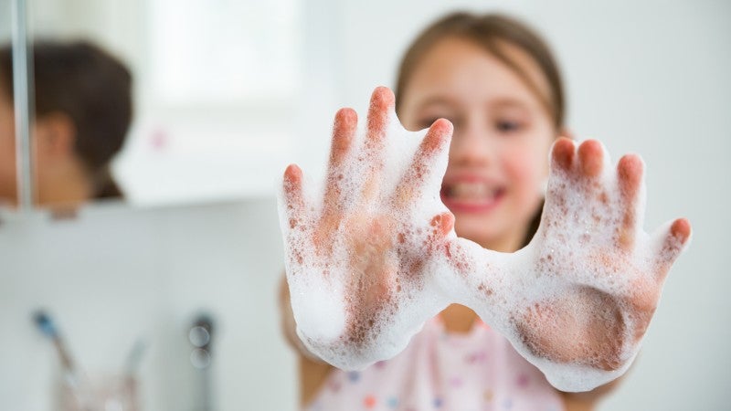 Glad flicka som tvättat händerna med massa tvålskum på händerna 