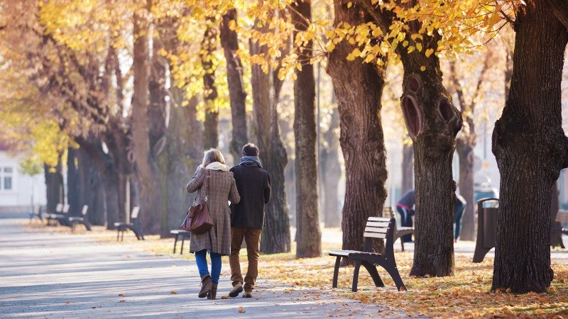 Medelålders par vandrar bland höstlöv i park