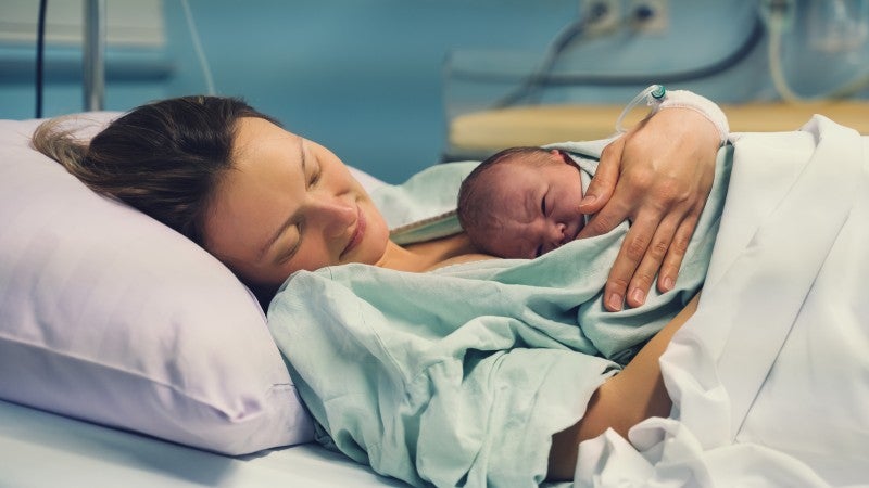 Kvinna på förlossningen med sin nyfödda bebis på magen