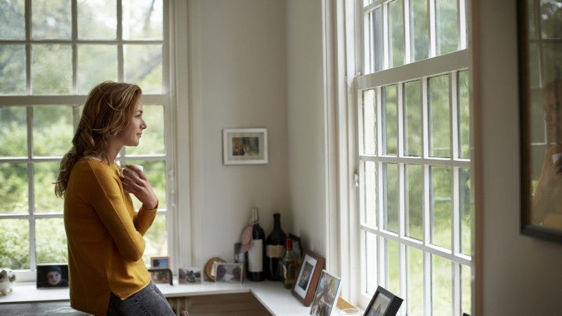 Kvinna håller en kopp kaffe och tittar ut genom ett fönster
